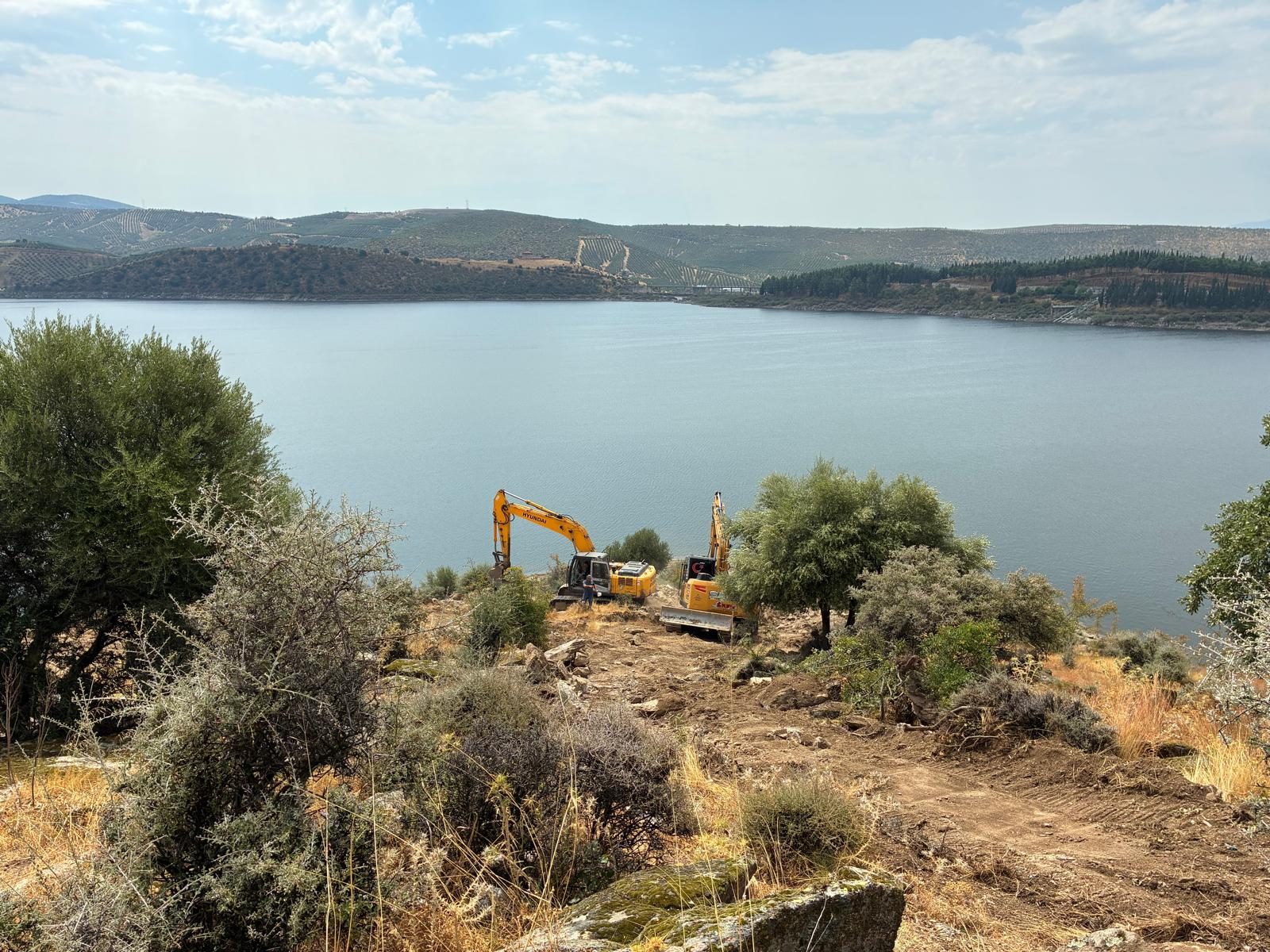 Demirköprü Barajı kıyısında enerji nakil hattı güzergâhında iş makineleriyle saha çalışması